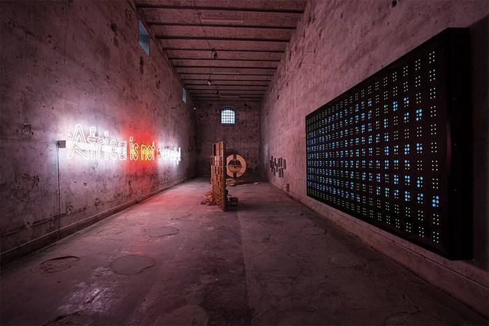 Room with red and white neon, circular wooden sculpture and framed drawings on the wall