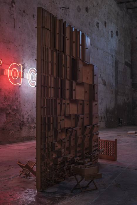 Vertical detail of a large wooden archive structure with drawers, neon visible in the background