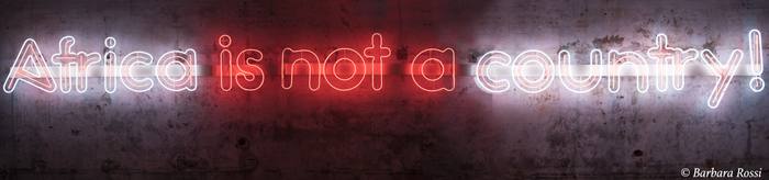 Red and white neon sign &laquo;Africa is not a country!&raquo; on a raw concrete wall