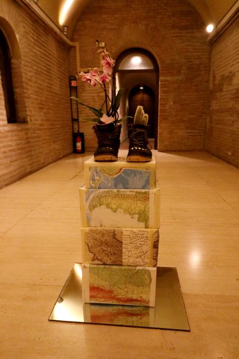 A pair of worn boots on a stacked pedestal, with an orchid growing from them