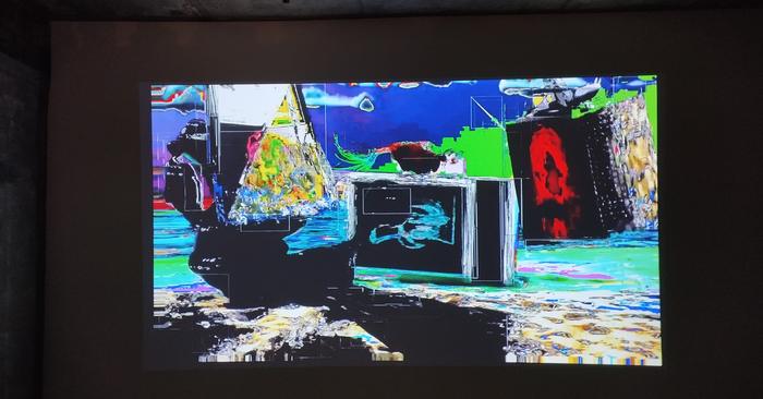 A colourful glitch-like video projected on a wall in a dark room