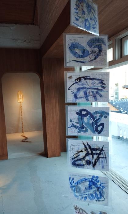 Transparent sheets with blue ink drawings hanging beside a window, and a rope installation in the corridor beyond