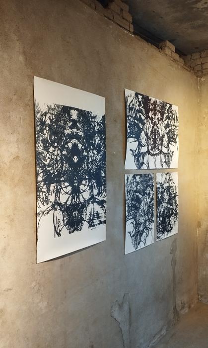 Four large black ink prints hung on a raw plaster wall