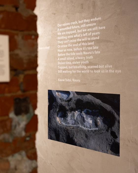 Wall text in white lettering on a plaster wall, a poem by Kauw Tsitsi, next to a macro photograph of a mineral surface
