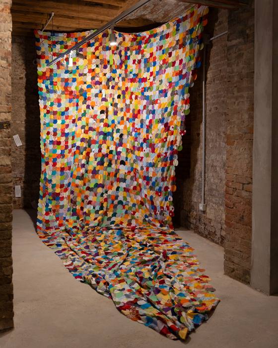 Large hanging patchwork curtain made of colourful fabric circles, pooling on the floor of a brick room