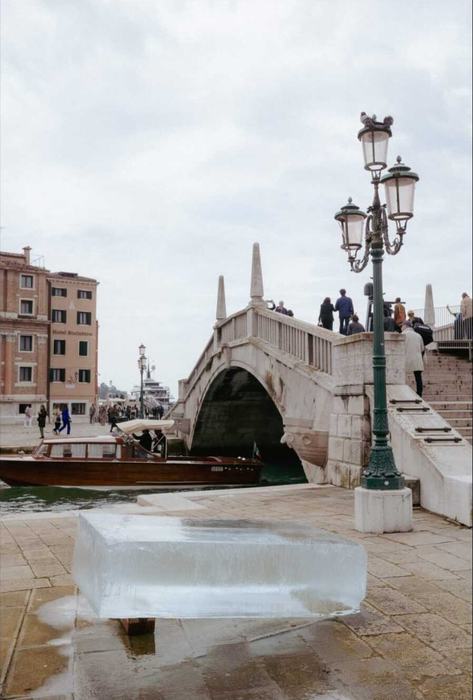 A block of ice on the quayside in Venice in front of a stone bridge and a green lamp post