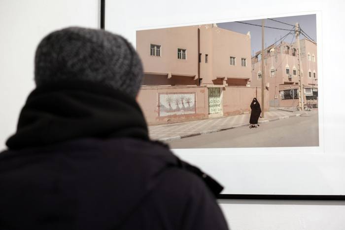 Visitatrice osserva una fotografia incorniciata di una strada in Marocco con una donna velata