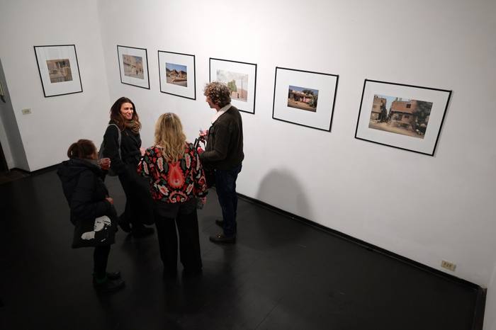 Camilla Boemio, di spalle, conversa con un gruppo di ospiti davanti a una fila di fotografie incorniciate