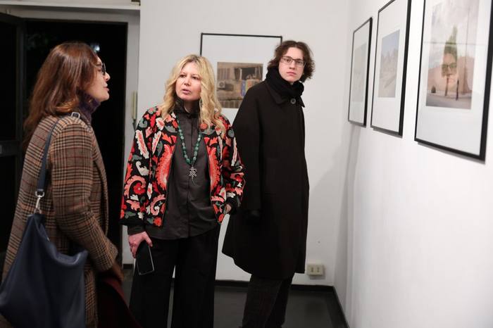 Camilla Boemio conversa con due ospiti vicino all&rsquo;ingresso della galleria, con una fotografia incorniciata alle spalle